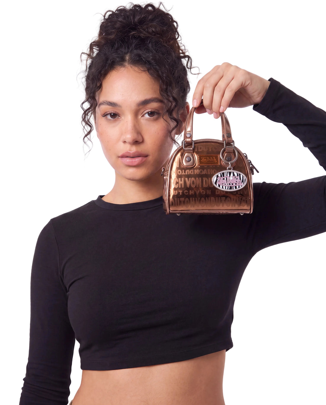 A woman in a black long-sleeve crop top holds up a small brown leather von dutch handbag